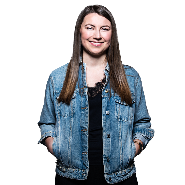 Porträt einer lächelnden Frau mit langen braunen Haaren und Jeansjacke vor neutralem Hintergrund.