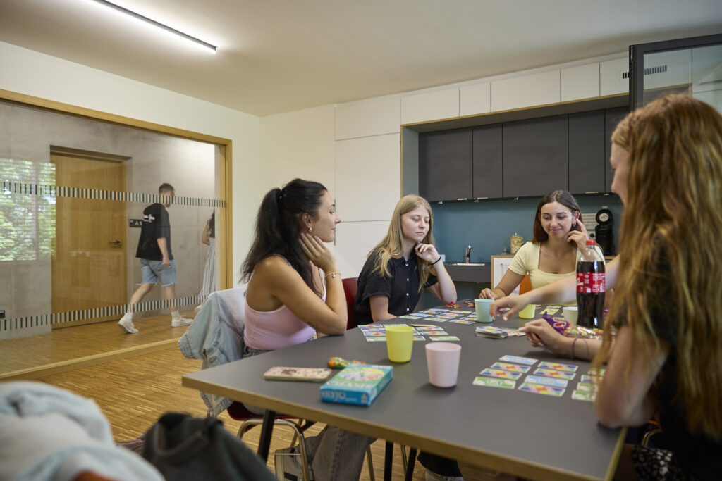 Vier Studentinnen sitzen in einem Aufenthaltsraum am Tisch und spielen ein Kartenspiel.