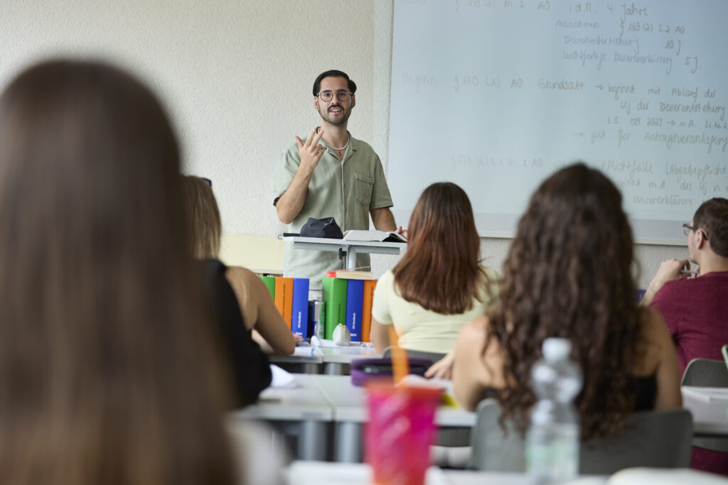 Dozent steht vor einer Klasse und erklärt den Unterrichtsstoff.