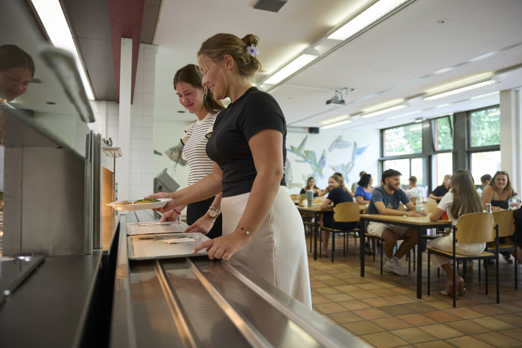 Zwei Studentinnen holen sich Essen an der Ausgabetheke einer Mensa.
